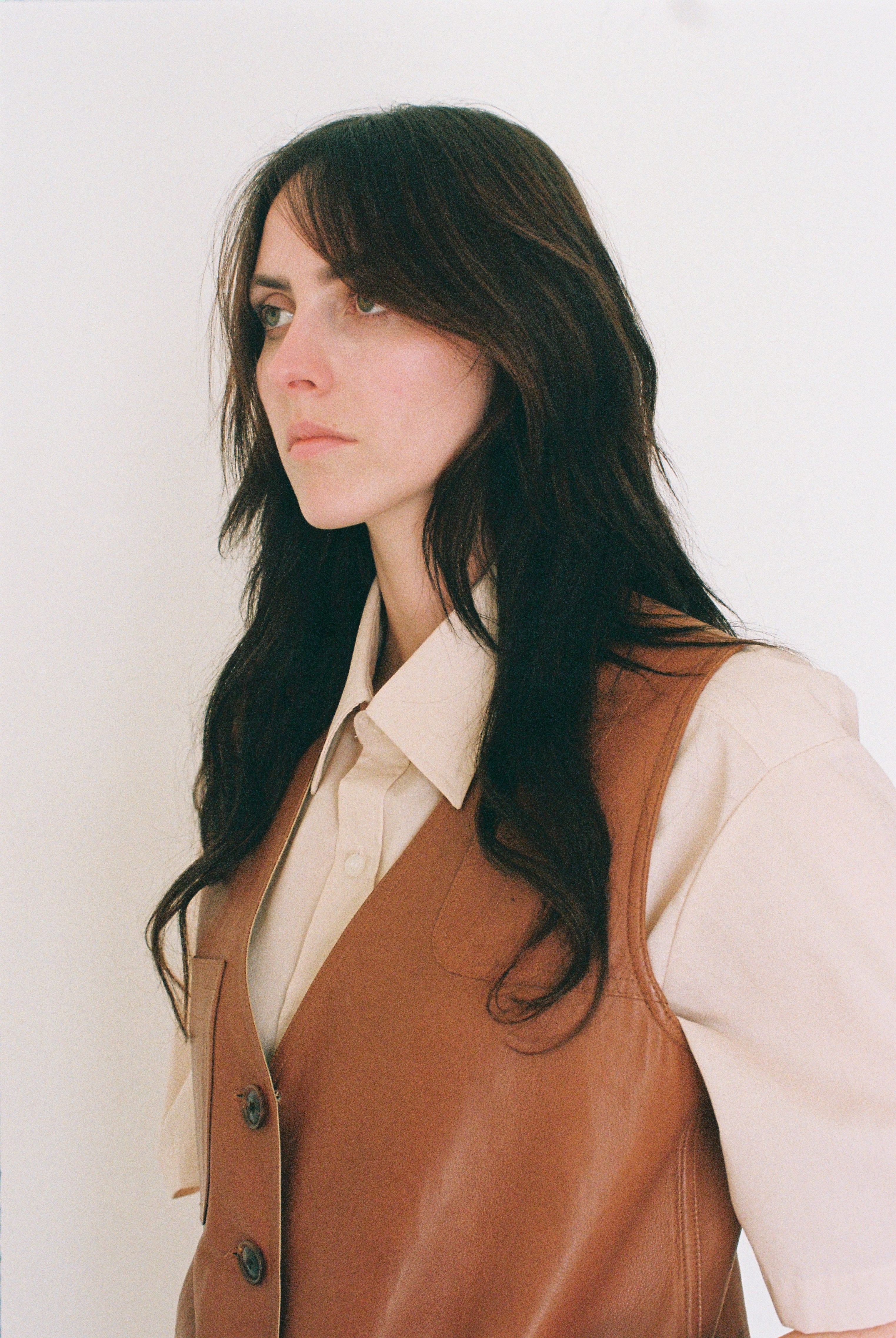 Woman wearing a brown vest over a beige shirt against a white background