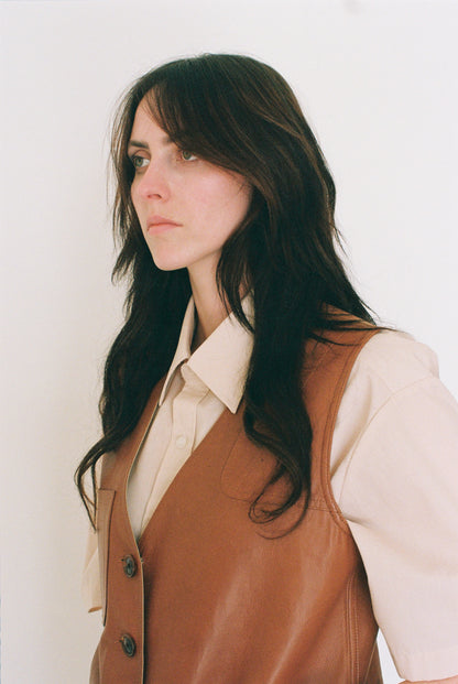 Woman wearing a brown vest over a beige shirt against a white background