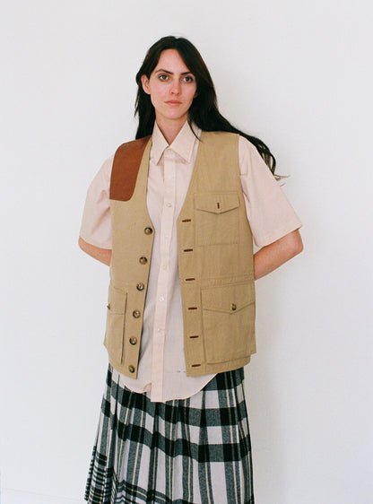 Woman wearing a beige vest over a white shirt and plaid skirt on a white background
