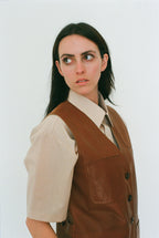 Woman wearing a brown vest over a beige shirt against a white background