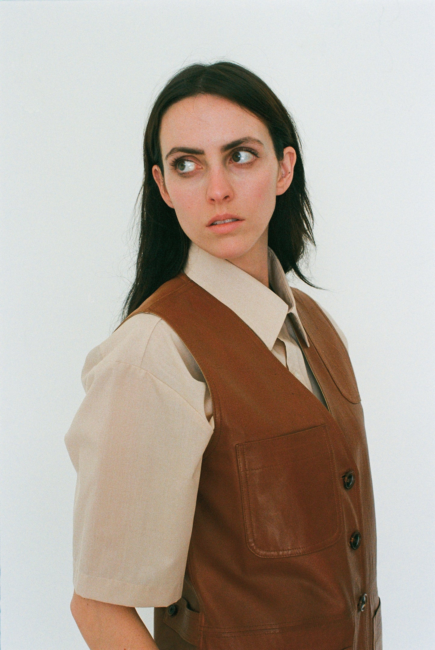 Woman wearing a brown vest over a beige shirt against a white background