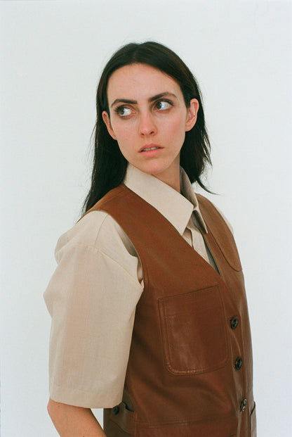 Woman wearing a brown vest over a beige shirt against a white background