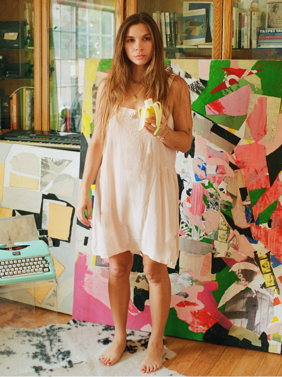Woman in a light dress holding a banana in front of colorful abstract art