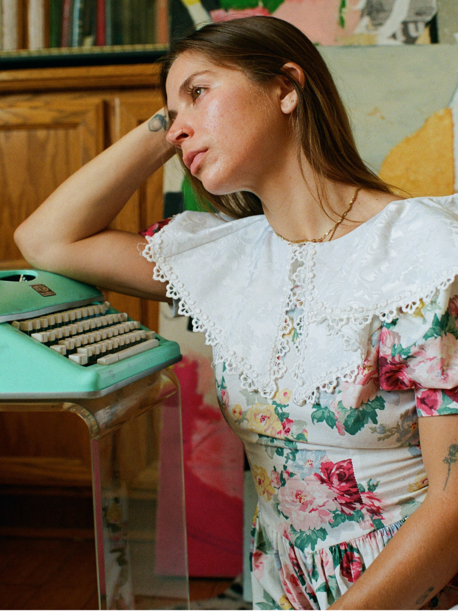 Woman in a floral dress sitting at a vintage turquoise typewriter.