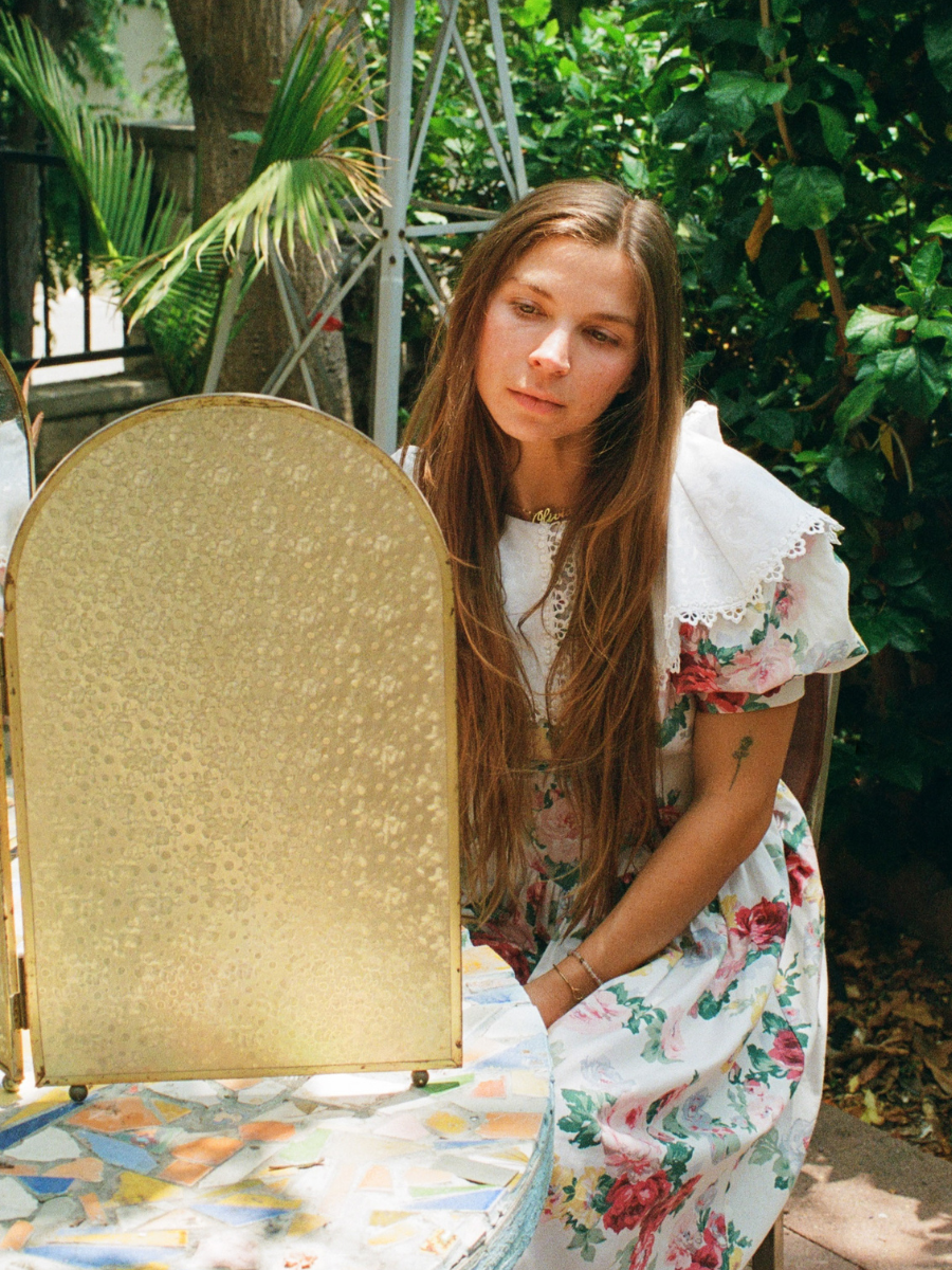 Woman in a floral dress sitting outdoors with a gold mirror