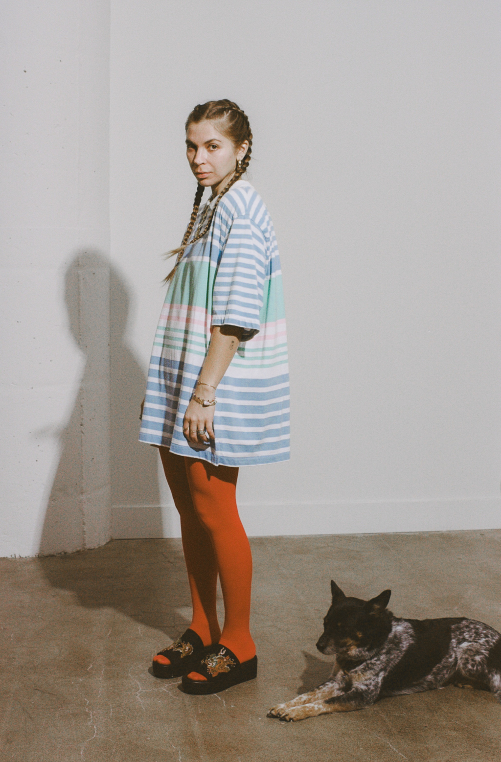Woman in a colorful striped dress standing next to a dog on a plain floor.