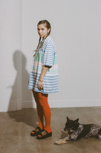 Woman in a colorful striped dress standing next to a dog on a plain floor.