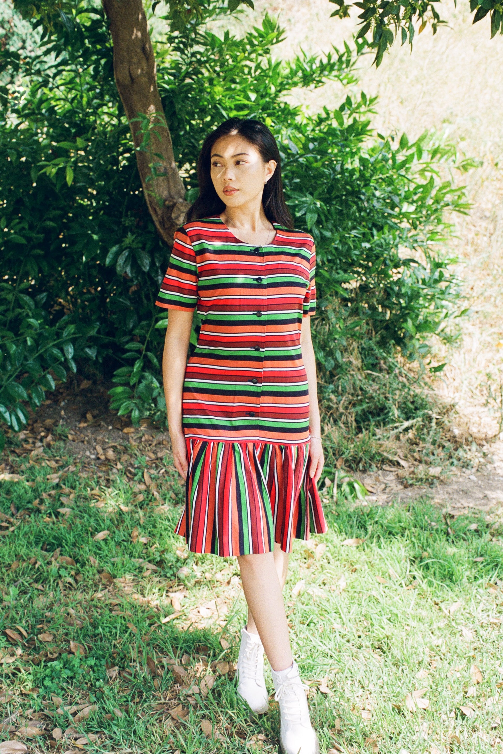 Woman wearing a colorful striped dress standing outdoors among greenery.