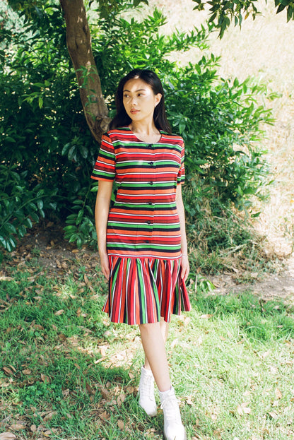 Woman wearing a colorful striped dress standing outdoors among greenery.