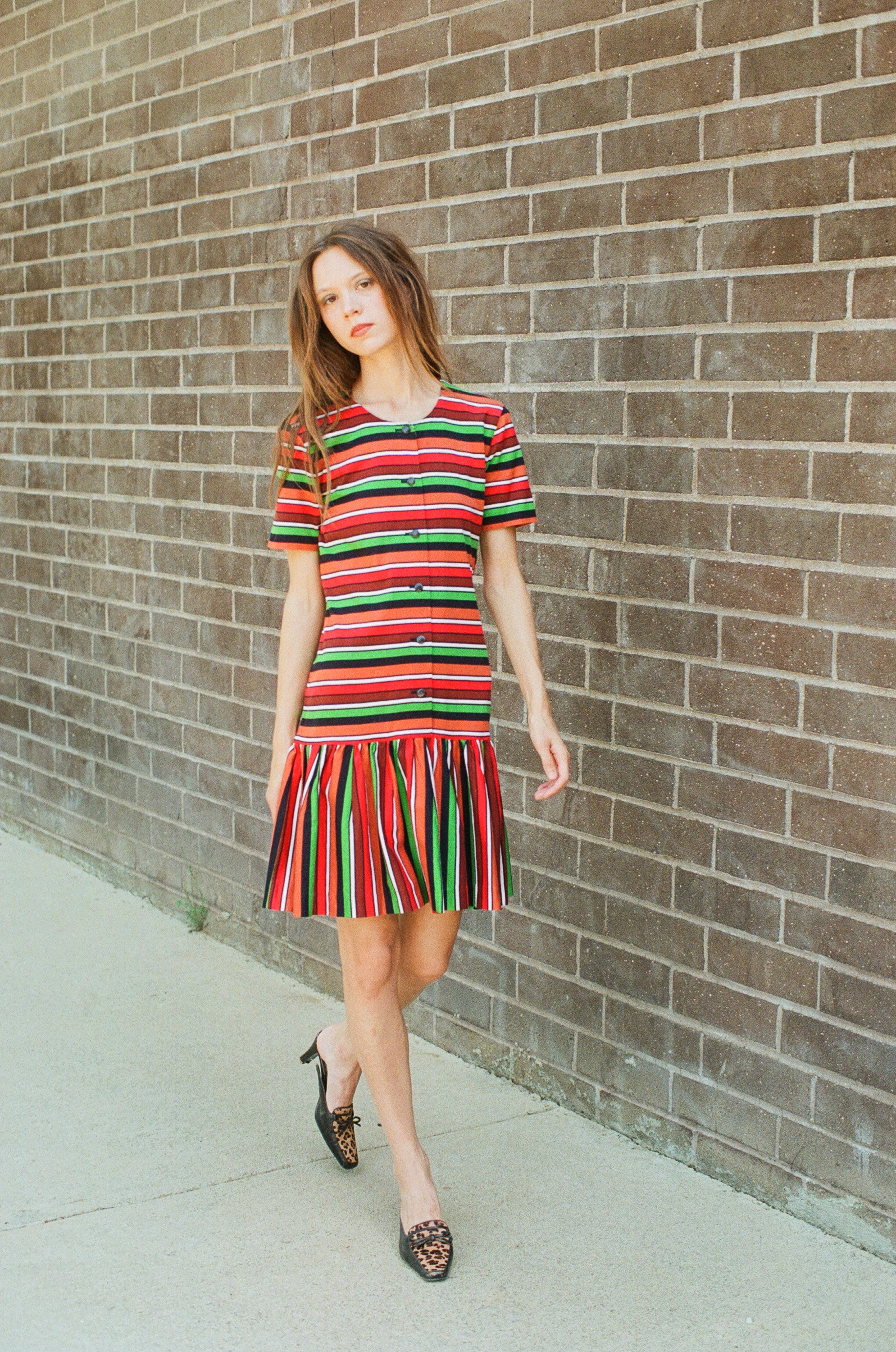 Woman wearing a colorful striped dress standing against a brick wall.