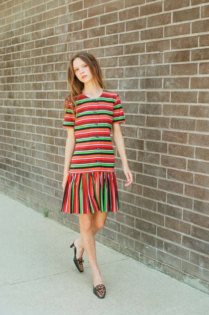 Woman wearing a colorful striped dress standing against a brick wall.