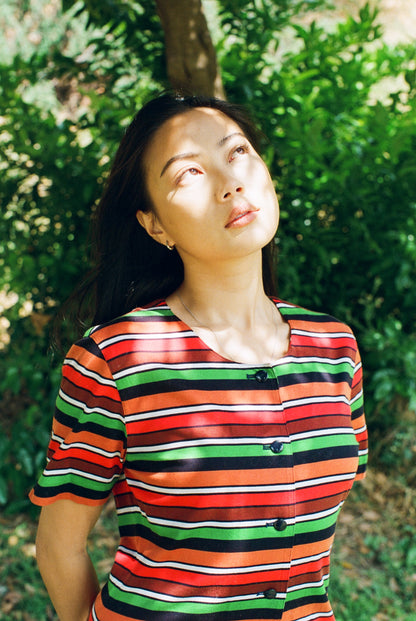Woman wearing a colorful striped shirt standing outdoors with greenery in the background