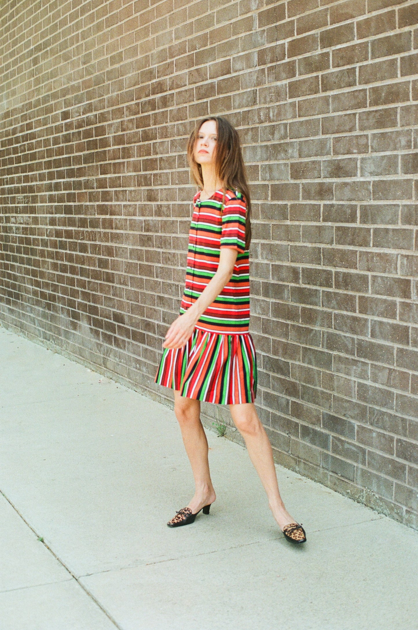 Woman in a red and green striped dress standing against a brick wall.