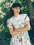 Woman wearing a floral dress standing in a natural setting with greenery.