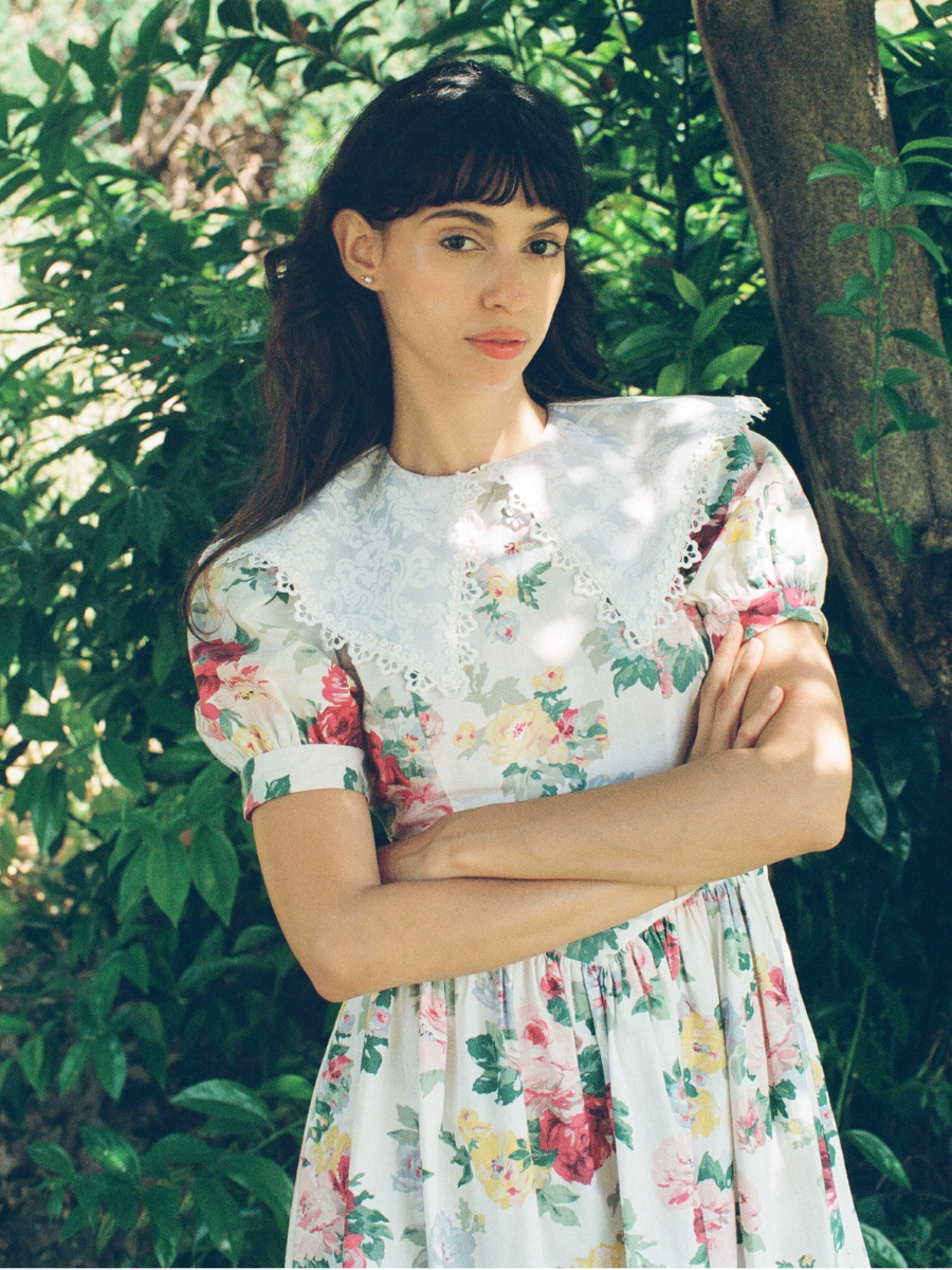 Woman wearing a floral dress standing in a natural setting with greenery.