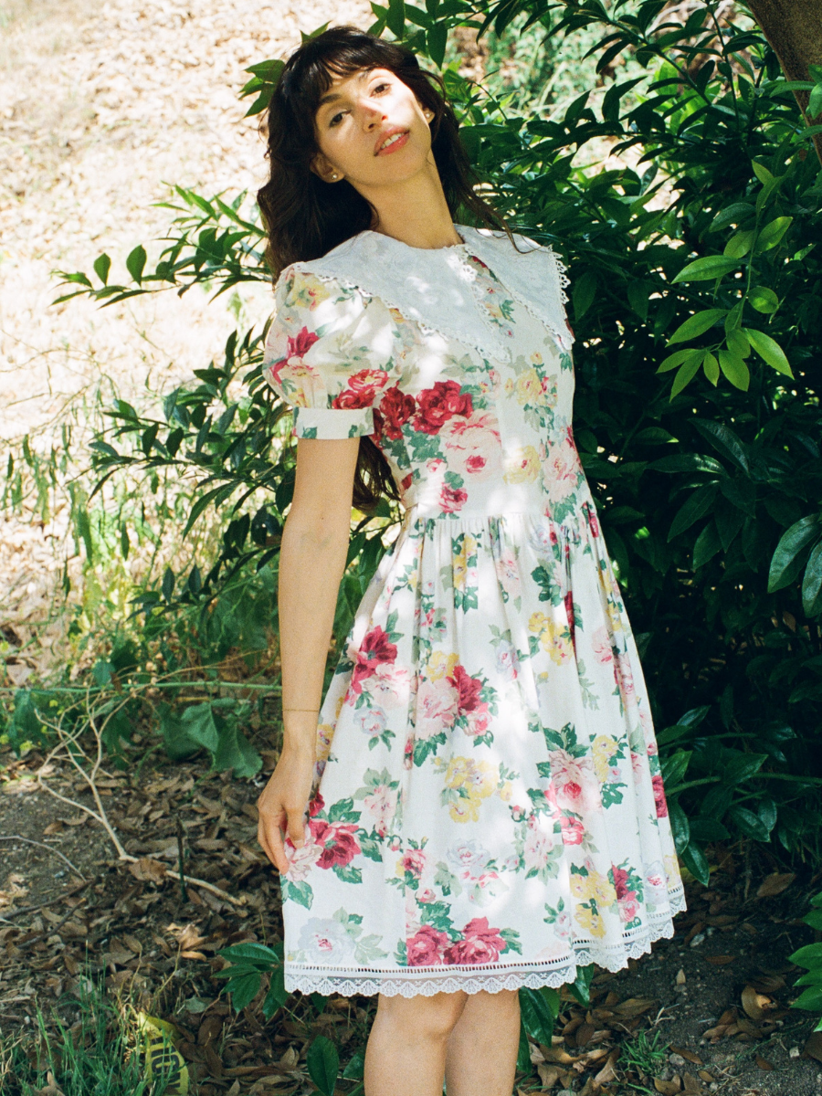 Woman wearing a floral dress standing in a natural setting with greenery.