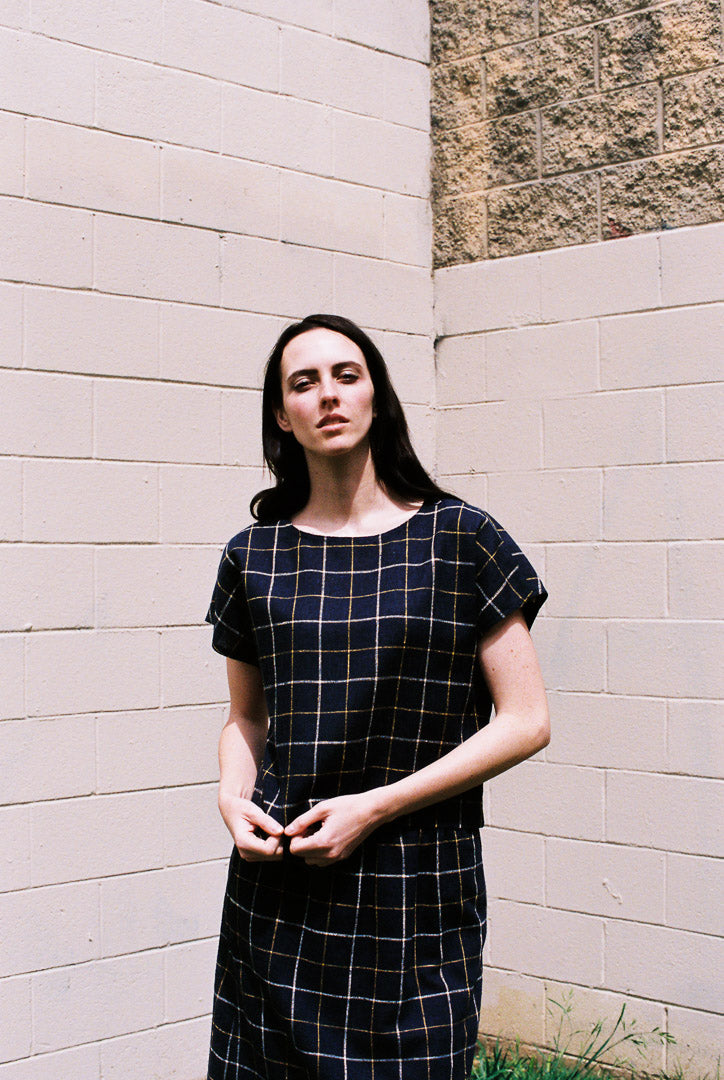 Woman wearing a black and white checkered dress standing against a light-colored wall.