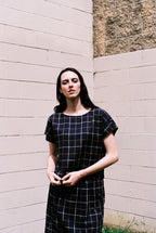 Woman wearing a black and white checkered dress standing against a light-colored wall.