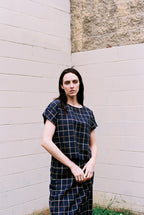 Woman wearing a black and white checkered outfit standing against a light-colored wall.