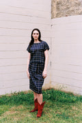 Woman wearing a plaid dress and red boots standing against a white wall.