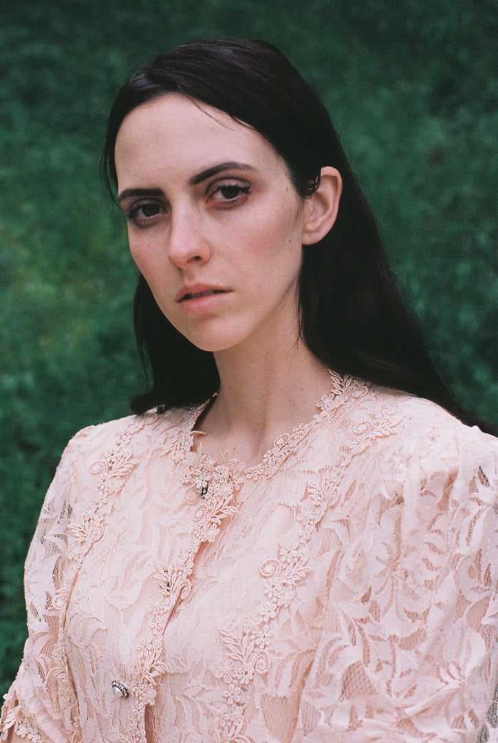 Woman wearing a beige lace top against a green background