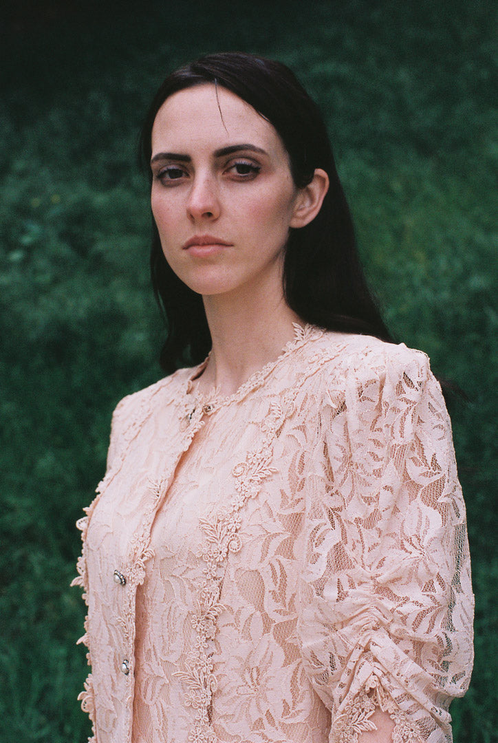Woman wearing a beige lace blouse against a green textured background