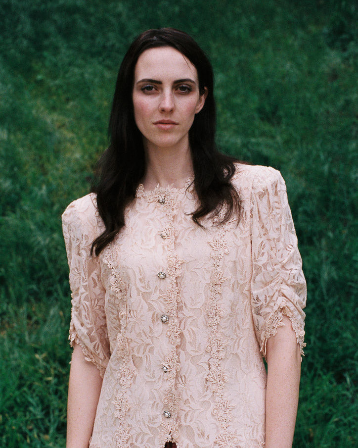 Woman wearing a beige lace blouse against a green background