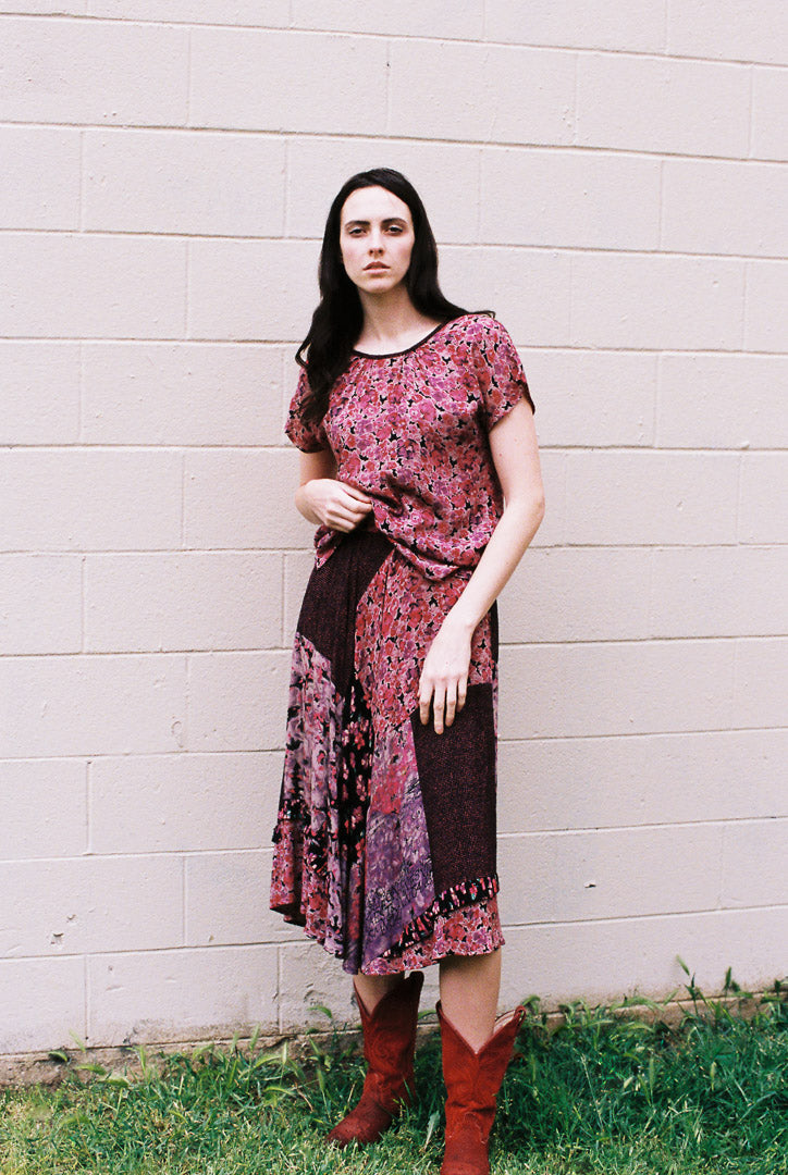 Woman wearing a patterned dress and red boots standing against a light-colored wall.