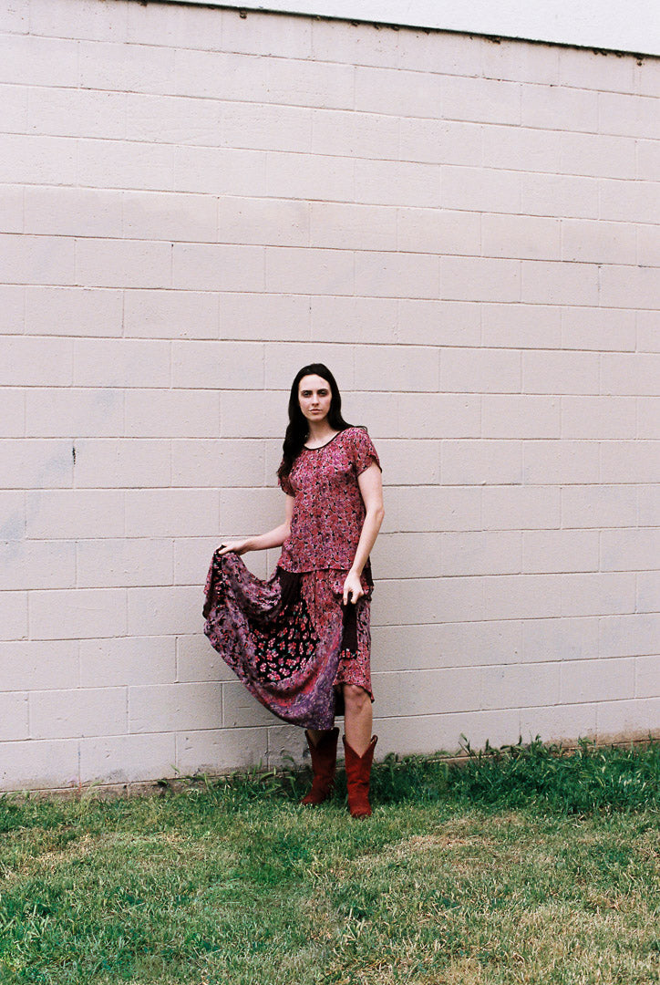 Woman in a patterned dress standing against a white wooden wall.