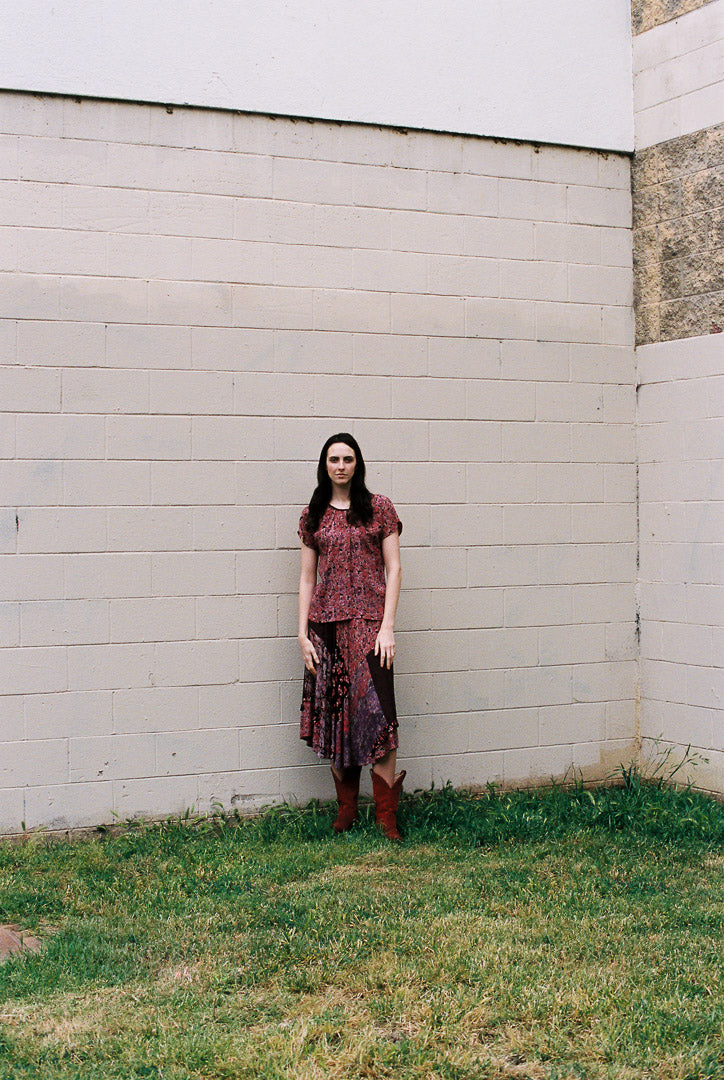 Woman standing against a white wall with grass at the base