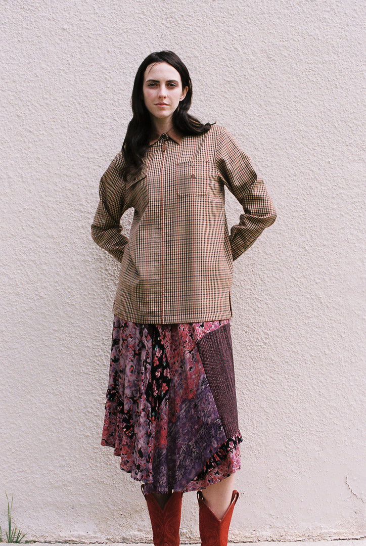 Woman wearing a plaid shirt and patterned skirt against a white wall