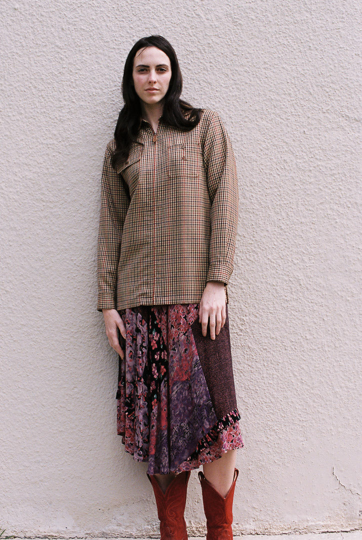 Woman wearing a patterned top and skirt against a textured wall.