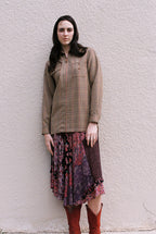 Woman wearing a patterned top and skirt against a textured wall.
