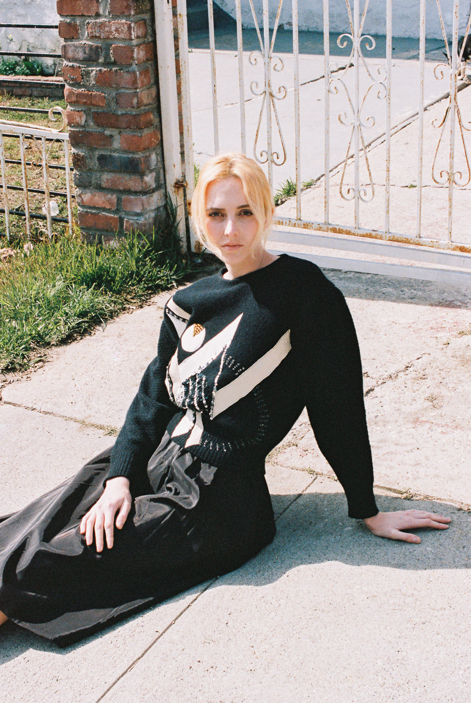 Woman sitting on a sidewalk wearing a black dress with a white stripe.