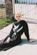 Woman sitting on a sidewalk wearing a black dress with a white stripe.
