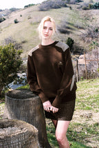 Person wearing a brown sweater with a geometric pattern in an outdoor setting