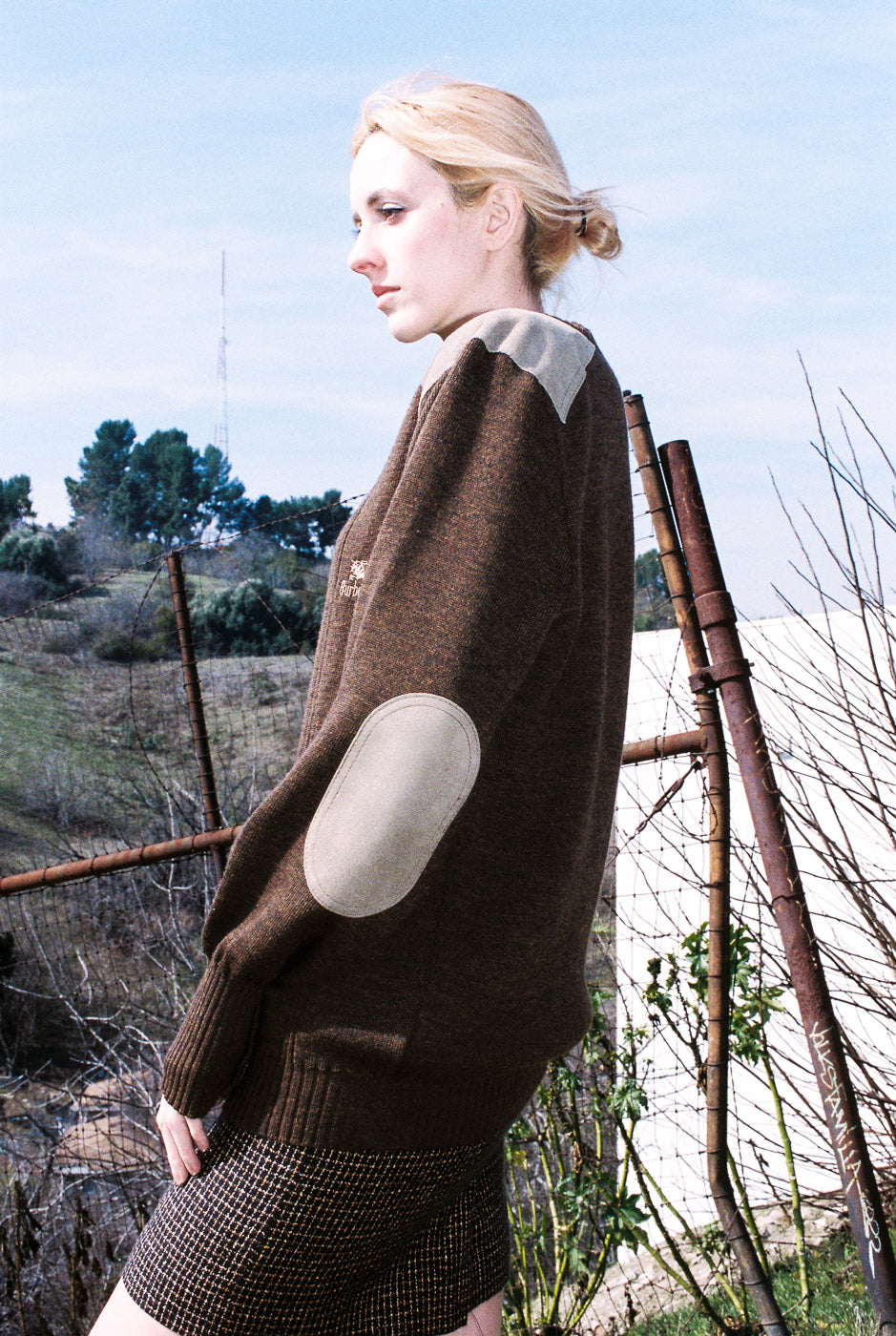 Woman wearing a brown sweater with a large circular patch outdoors.