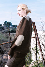 Woman wearing a brown sweater with a large circular patch outdoors.
