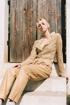 Woman in beige outfit sitting on steps with wooden door in background