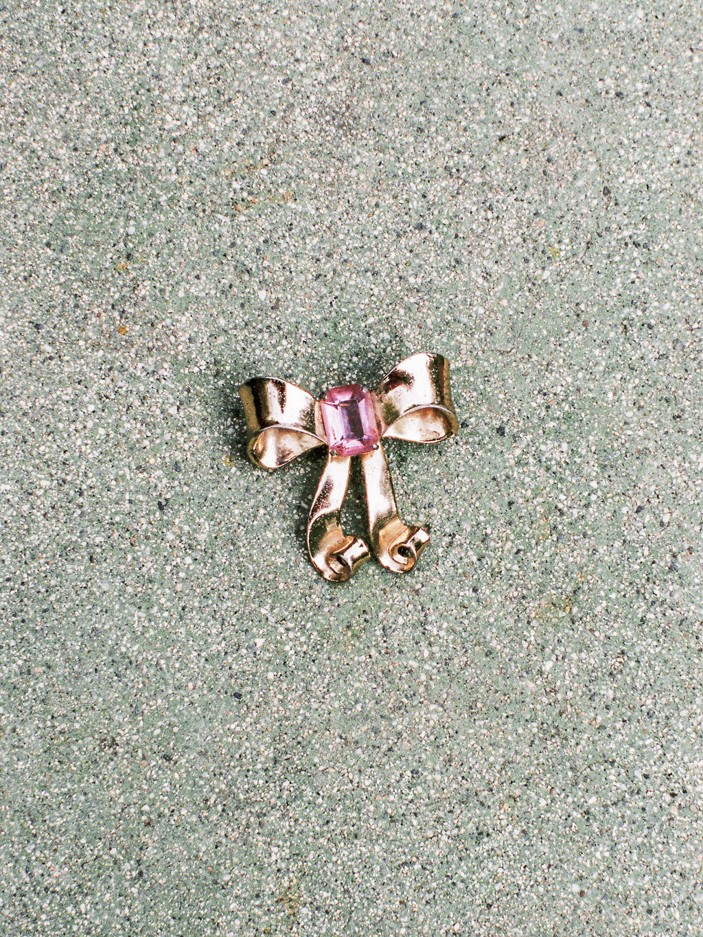 Gold bow-shaped jewelry with a pink gemstone on a textured surface