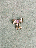 Gold bow-shaped jewelry with a pink gemstone on a textured surface