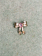 Gold bow-shaped jewelry with a pink gemstone on a textured surface