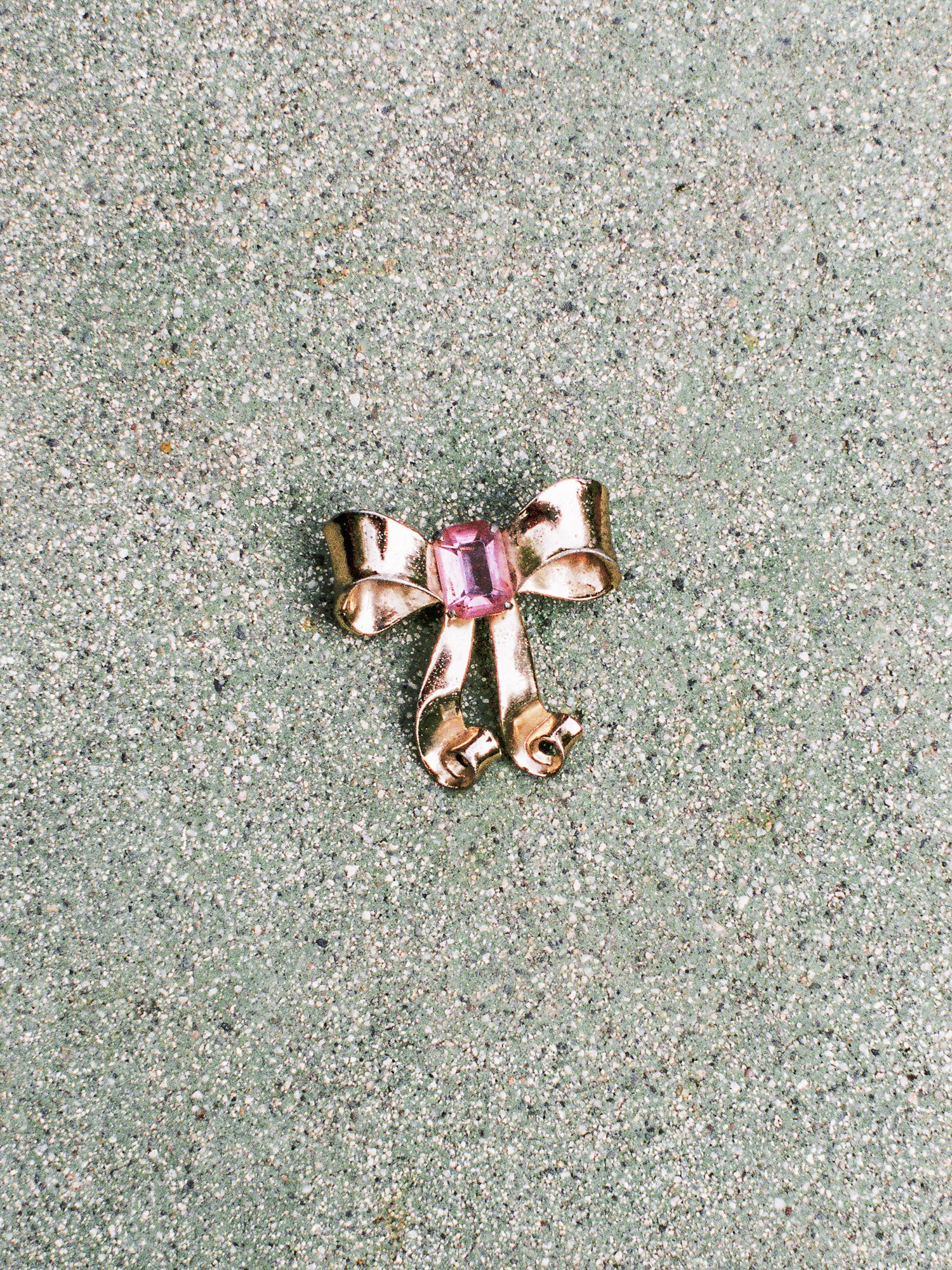 Gold bow-shaped jewelry with a pink gemstone on a textured surface