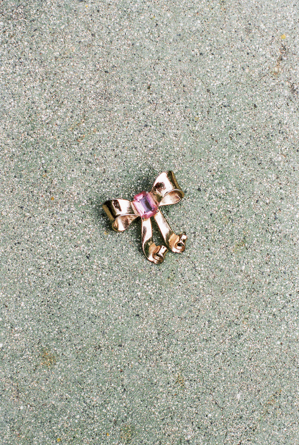 Gold bow-shaped brooch with pink gemstone on a textured surface