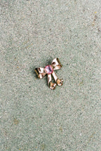 Gold bow-shaped brooch with pink gemstone on a textured surface