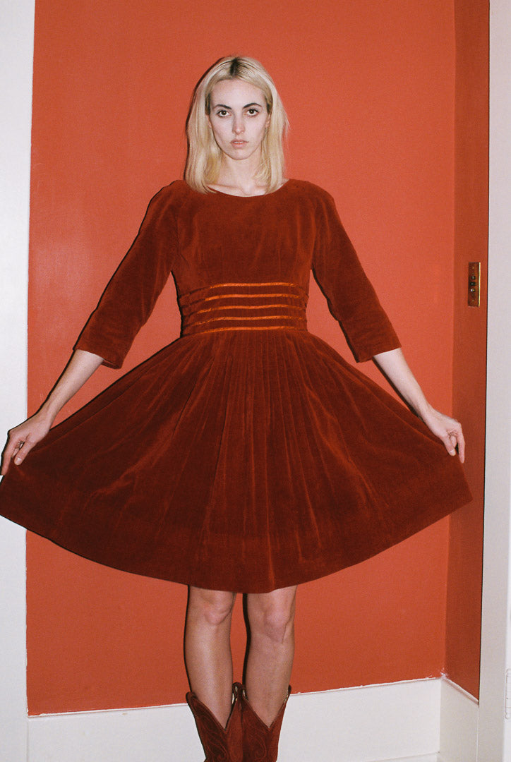 Woman wearing a brown velvet dress against an orange wall.