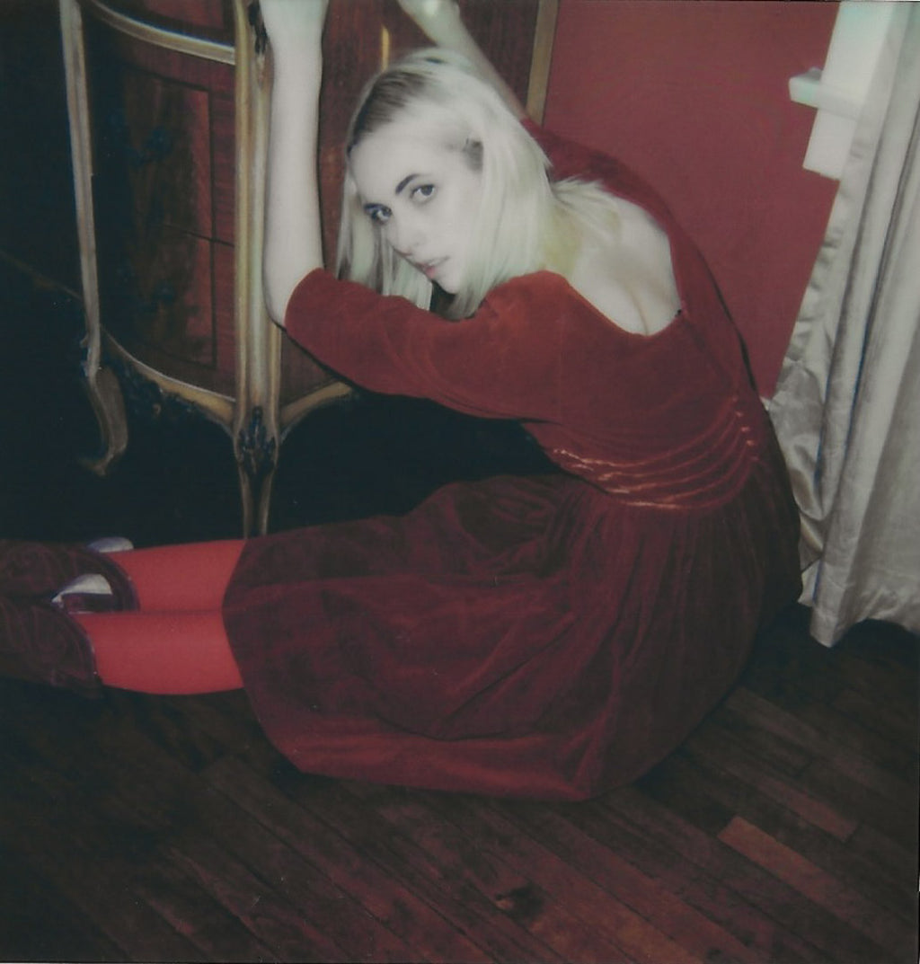 woman in a red dress sitting on the floor in a dimly lit room.