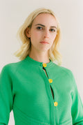 Woman wearing a green cardigan with yellow buttons against a white background