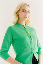 Woman wearing a green cardigan with yellow buttons against a white background