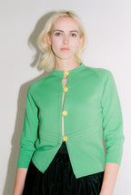 Woman wearing a green cardigan with yellow buttons against a plain background